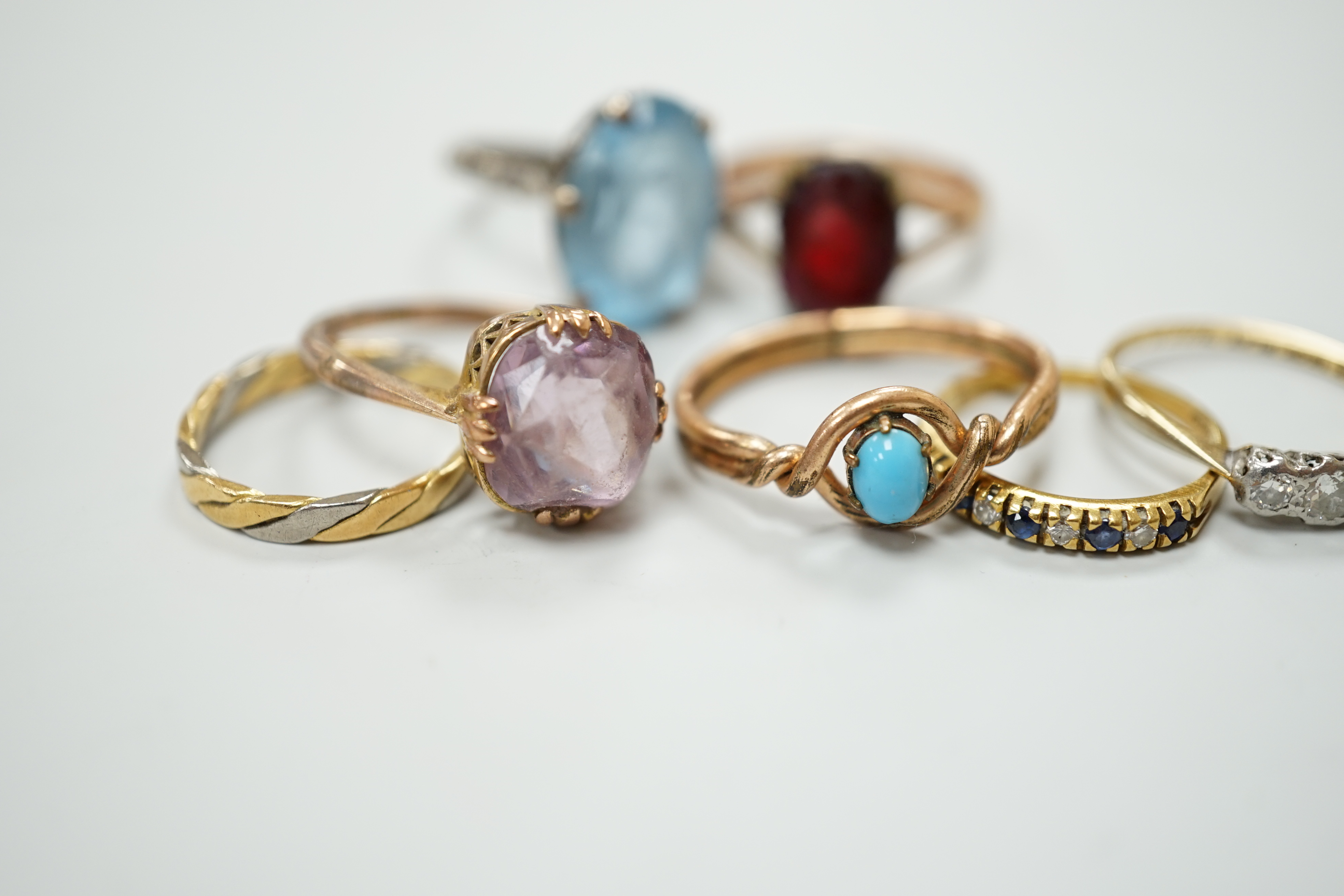 Seven assorted dress rings, comprising an 18ct gold three stone diamond ring, size M, a 9ct gold dress ring with associated worn red stone, size P, a silver ring with blue stone, size I, a 9ct gold and amethyst ring, siz